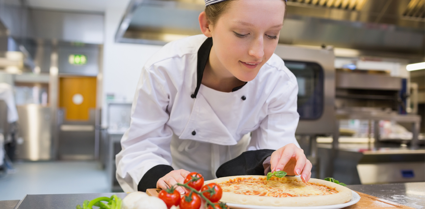 Young chef smiles as she makes finishing touches to her pizza with some fresh basil leaves